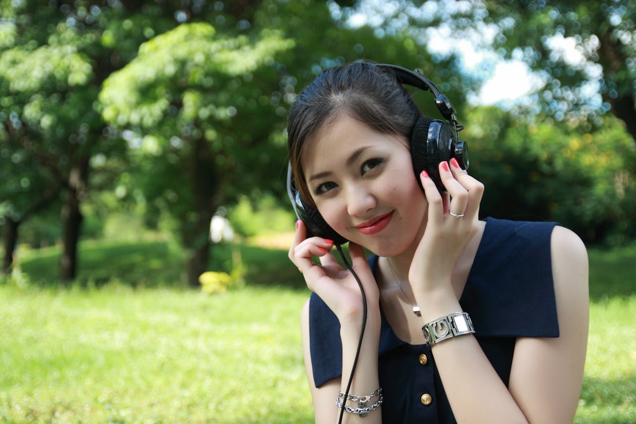 Smiling young woman listening to music with headphones in a sunny park.