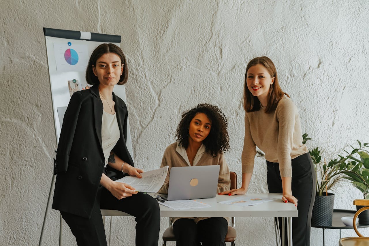 Team of women working together in an office setting with charts and laptop.